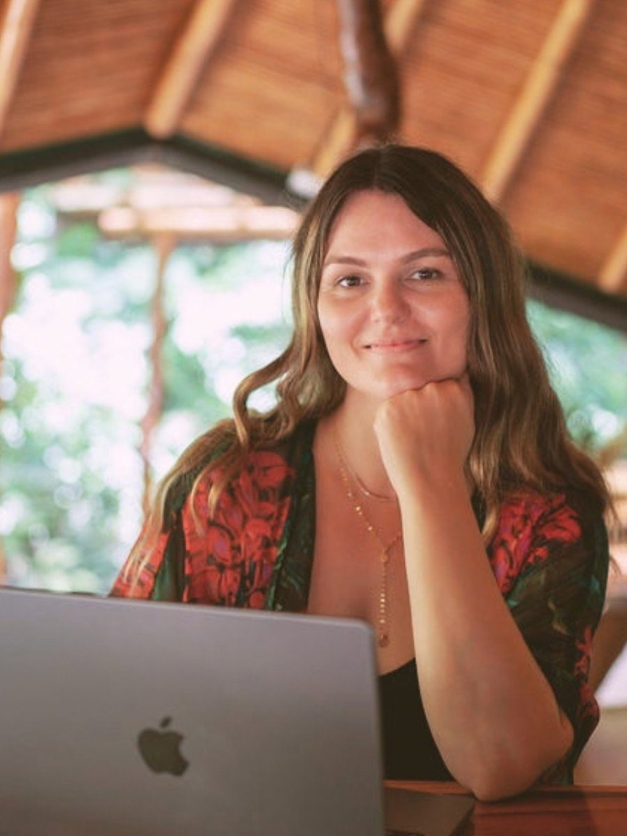 Selina smiling at her laptop in an open-air jungle studio